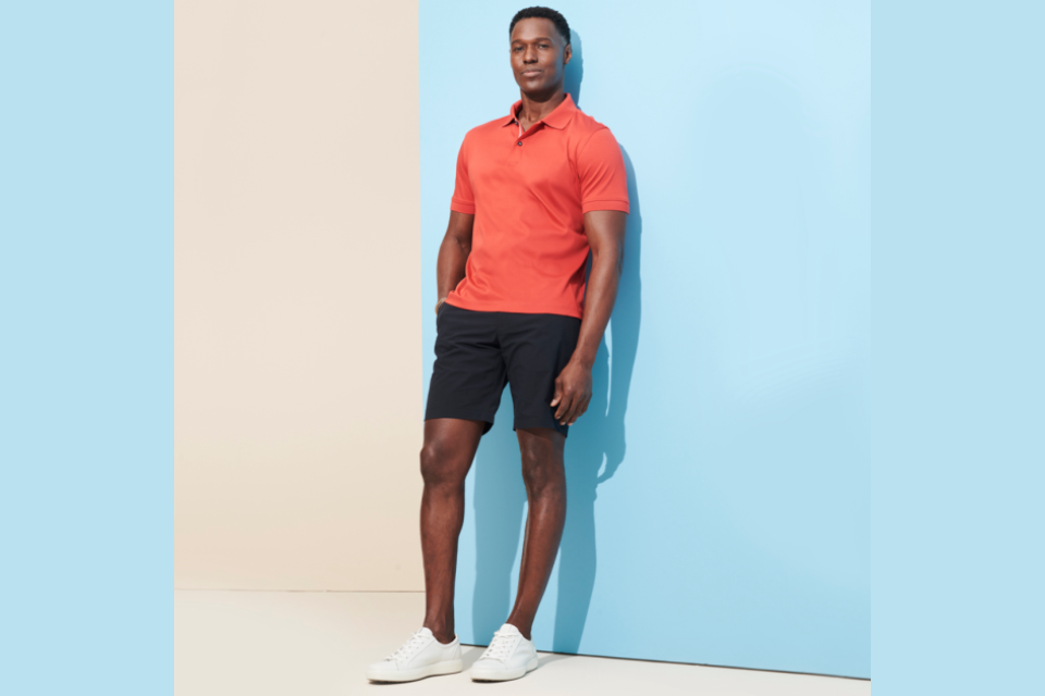 man in orange shirt and black shorts standing in front of light blue wall