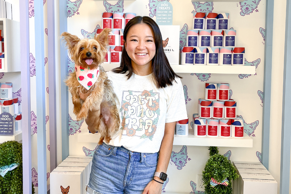 girl holding small dog in front of shelf with dog treats in colorful packaging