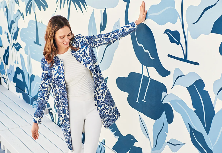 woman in white pants and blue floral coat in front of blue floral wall